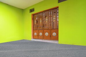 A room with a bright green wall, a grey carpeted floor, and a wooden door with decorative metal handles.
