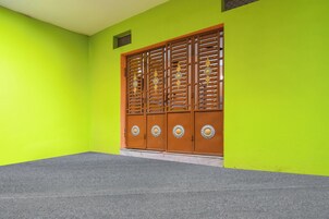 Une pièce avec un mur vert vif, un sol recouvert d’un tapis gris et une porte en bois dotée de poignées métalliques décoratives.