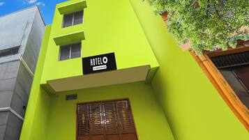 A building with a bright green facade, a sign indicating it's a hotel, and a wooden door with a window.