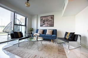 A modern living room with a glass coffee table, a blue sofa, and two black armchairs. - Bloomfields 1BR Duplex in Raha Lofts 2  (Abu Dhabi)