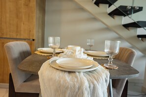 A dining table set with plates, glasses, and a candle, with a staircase in the background. - Bloomfields 1BR Duplex in Raha Lofts 2  (Abu Dhabi)
