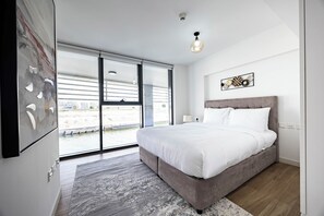A modern bedroom with a large bed, a view of a river through floor-to-ceiling windows, and a ceiling light fixture. - Bloomfields 1BR Duplex in Raha Lofts 2  (Abu Dhabi)