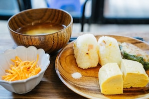 Una mesa de madera con un tazón de sopa, un plato con bolas de arroz, queso rallado y un vegetal verde.