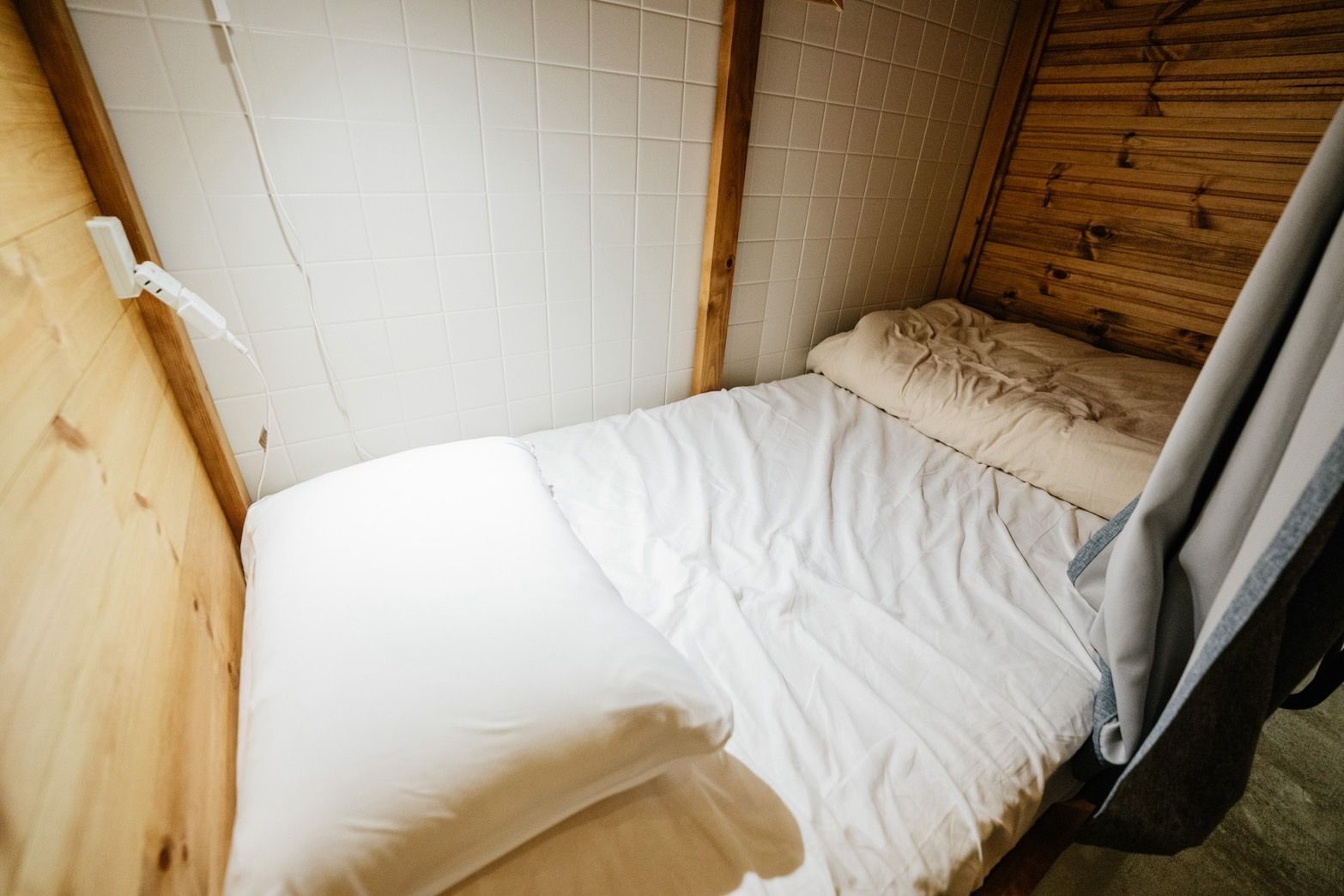 A small, compact room with a single bed, a wooden headboard, and a tiled wall.