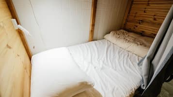 A small, compact room with a single bed, a wooden headboard, and a tiled wall.