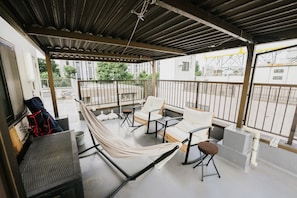 Een overdekt balkon met een hangmat, twee witte fauteuils met kussens en een klein krukje.
