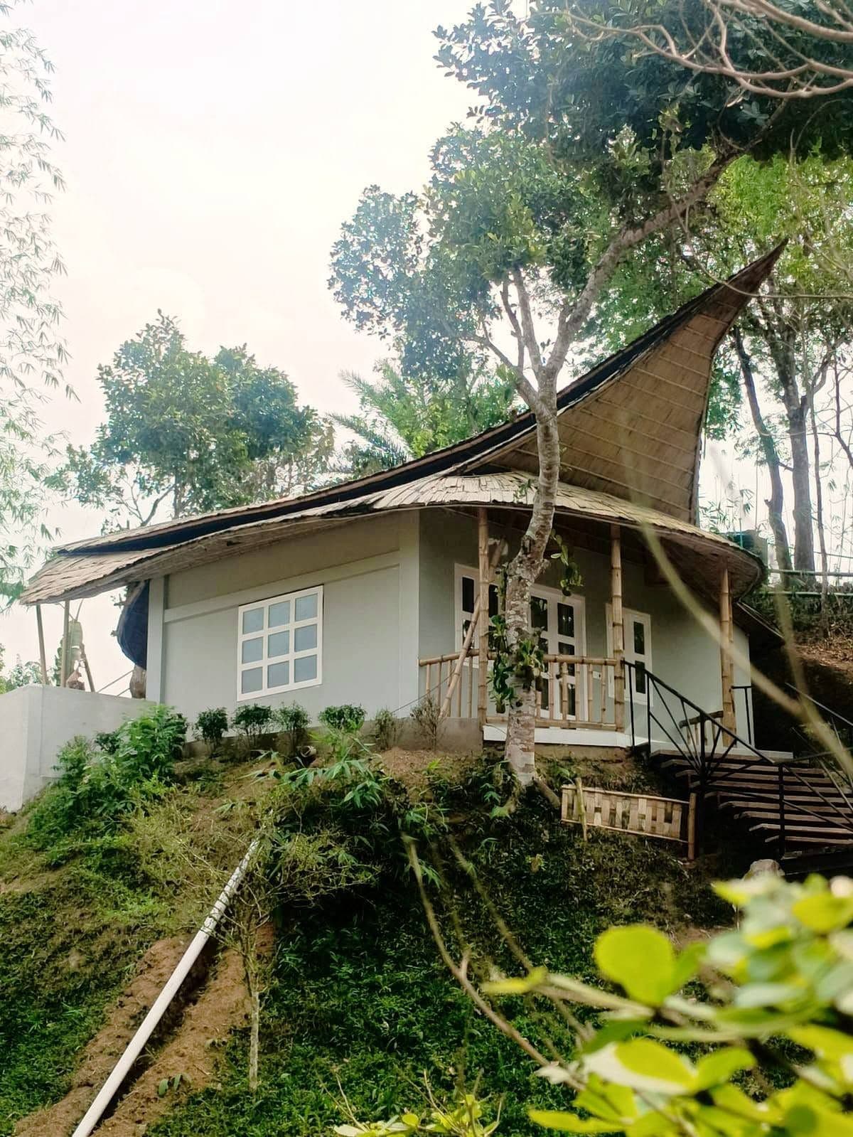 Uma casa com telhado curvo, escadaria que leva a um alpendre, e vista para o verde ao redor.