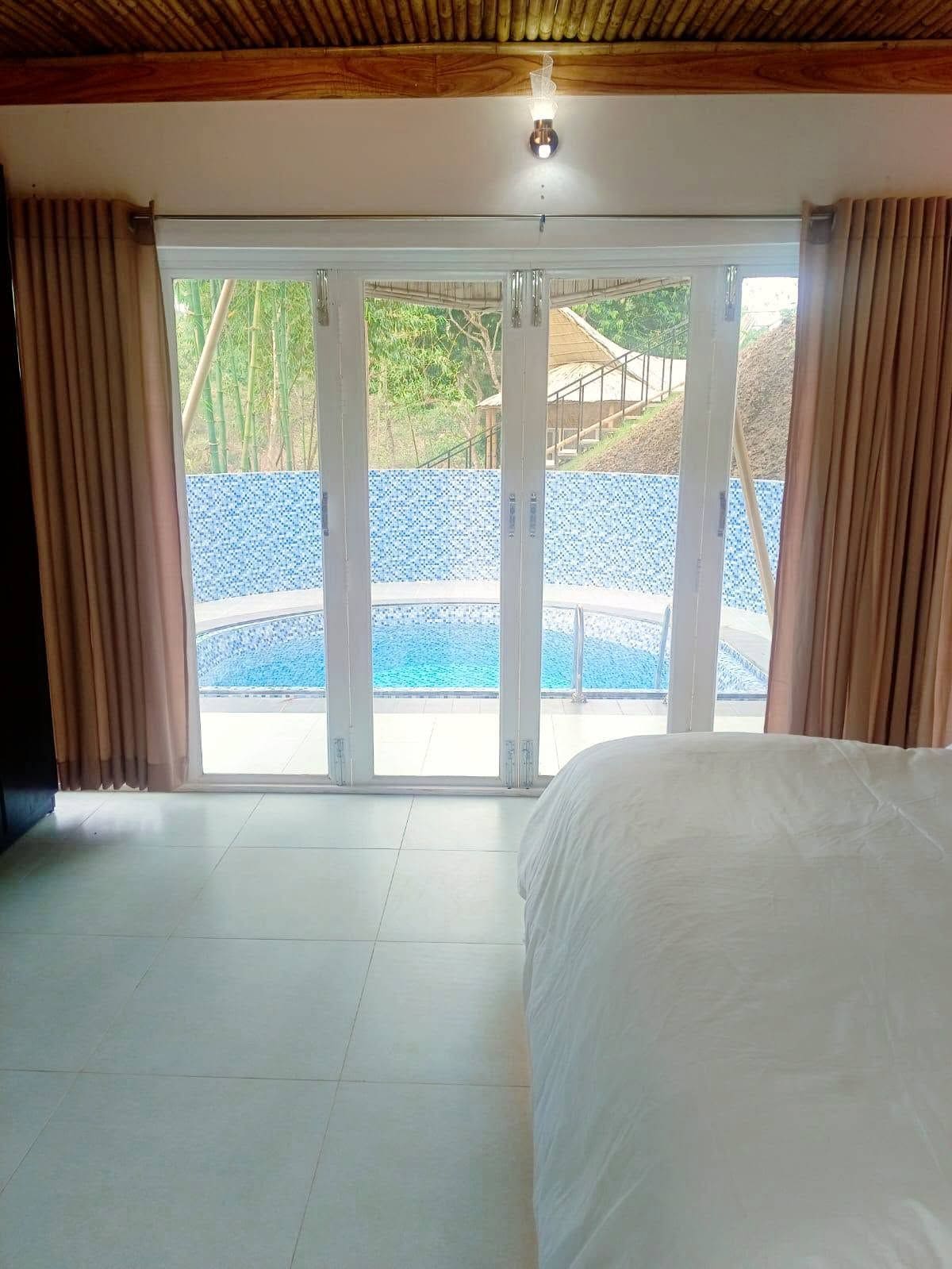 Quarto com uma cama grande, vista para uma piscina e teto de madeira.