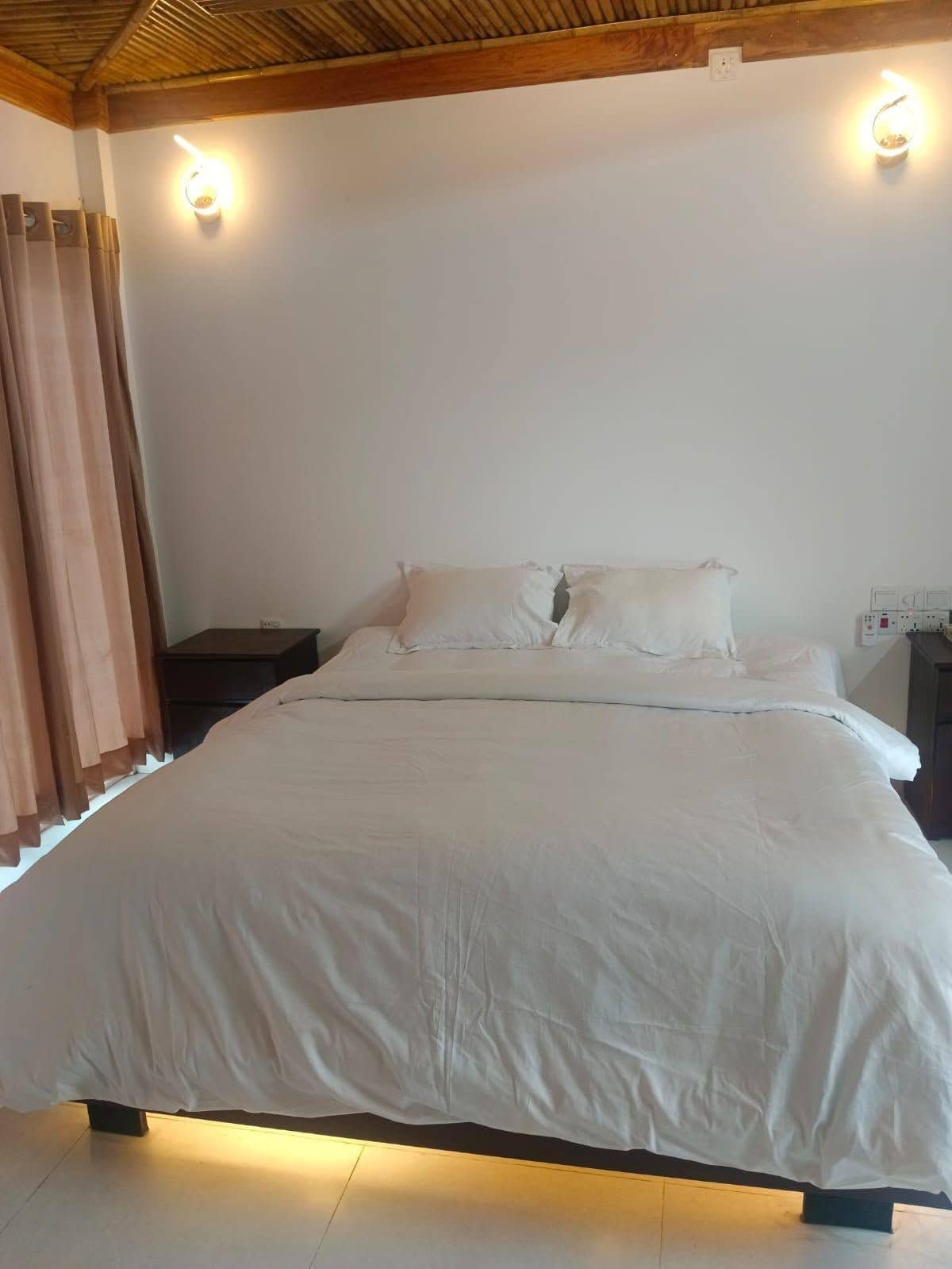 A bed with white bedding, a wooden ceiling, and two wall-mounted light fixtures.