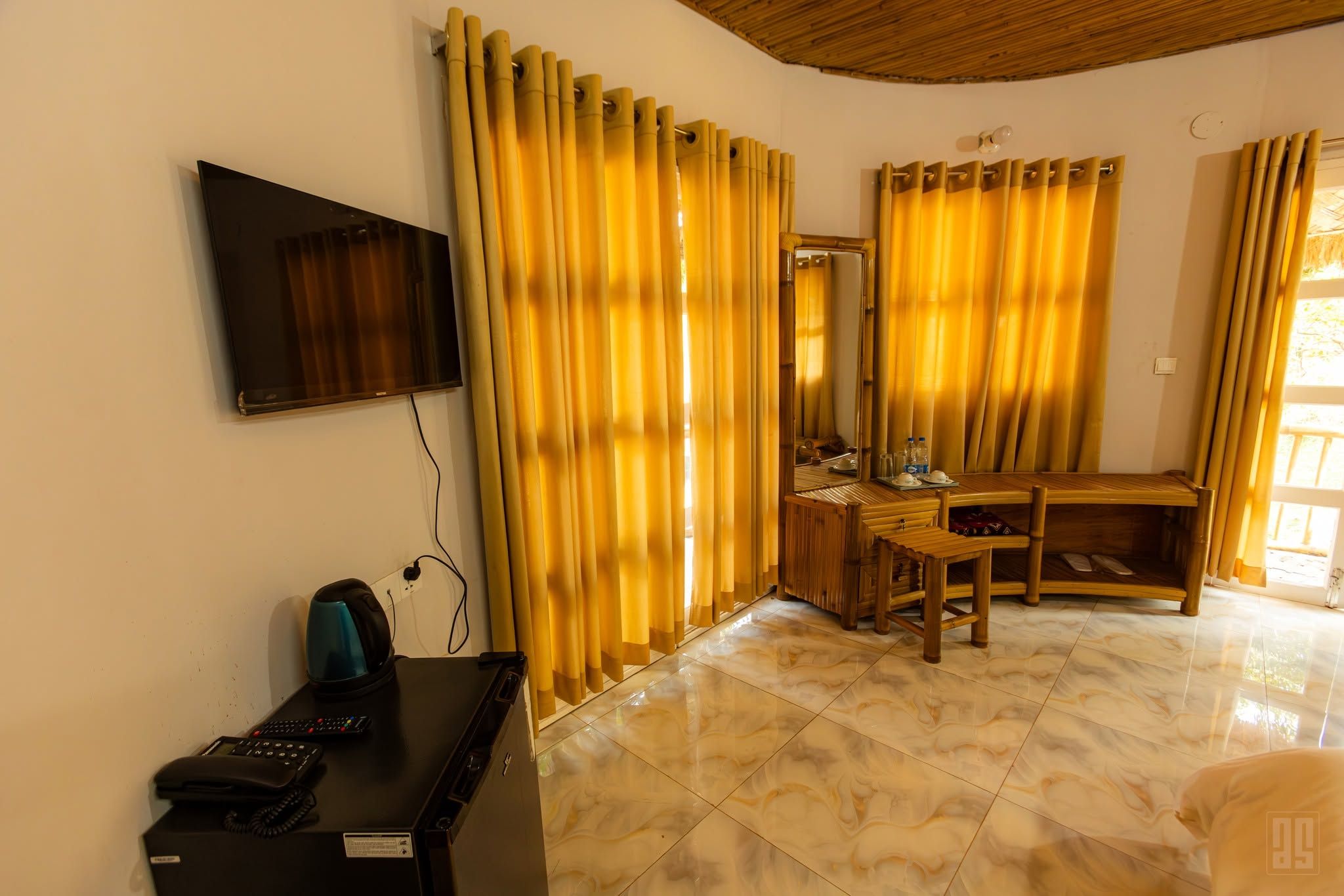 Una habitación con televisión montada en la pared, un escritorio con computadora, una silla y una cama con cabecera.