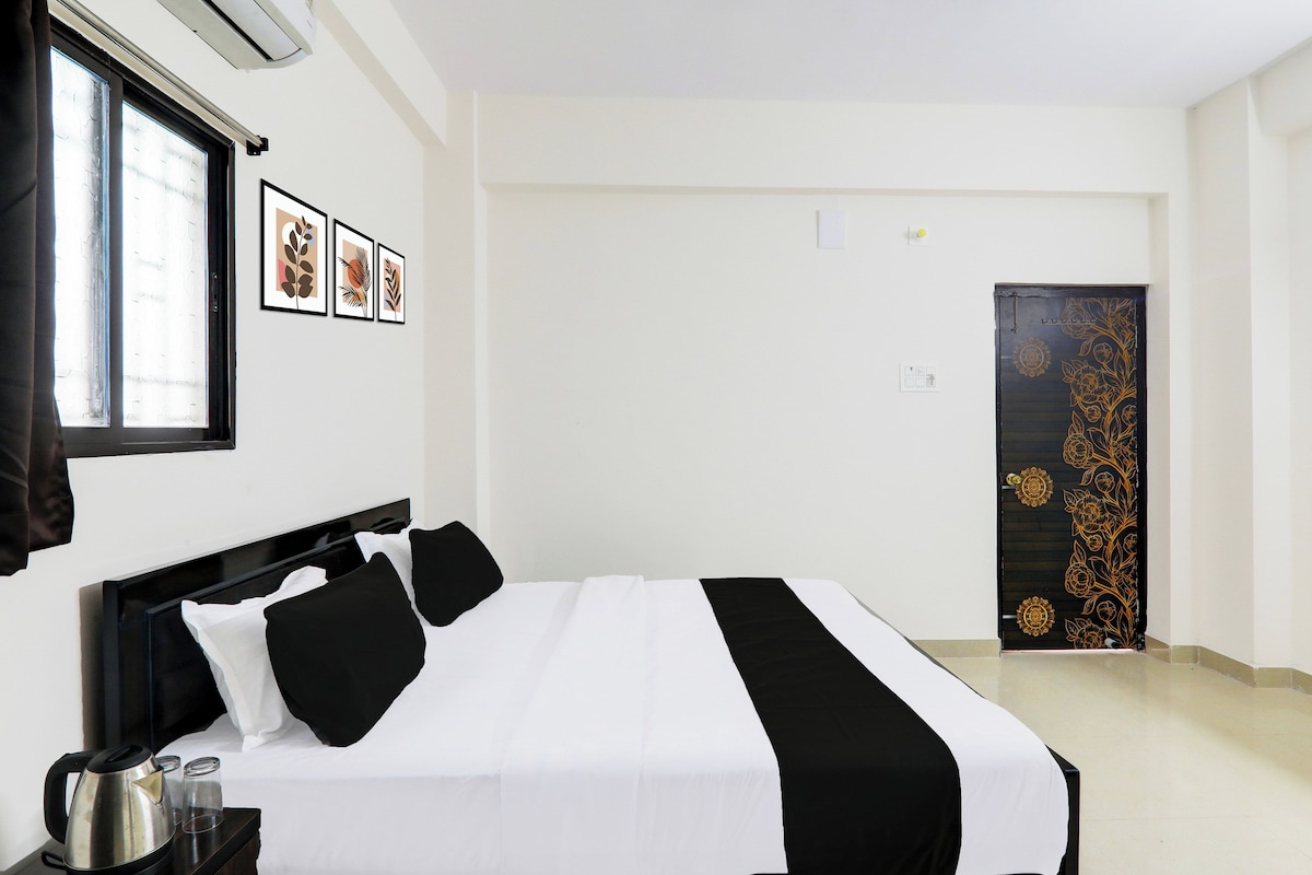 Una habitación de hotel con cama, ventana con persianas, puerta con panel decorativo y aire acondicionado de pared.
