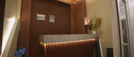 A reception desk with a wooden panel design, a security camera, and a sign indicating check-in and check-out times.
