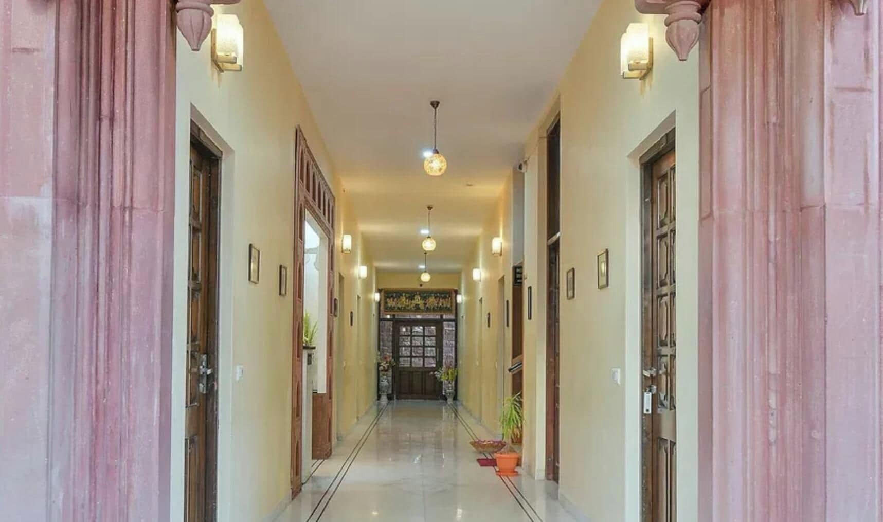Un pasillo con puertas a ambos lados, piso de baldosas y luces en la pared.