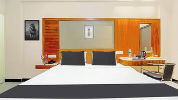 Een hotelkamer met een groot bed, een nachtkastje met een telefoon en een bloevas, een spiegel en een bureau met een waterkoker en een fles water.