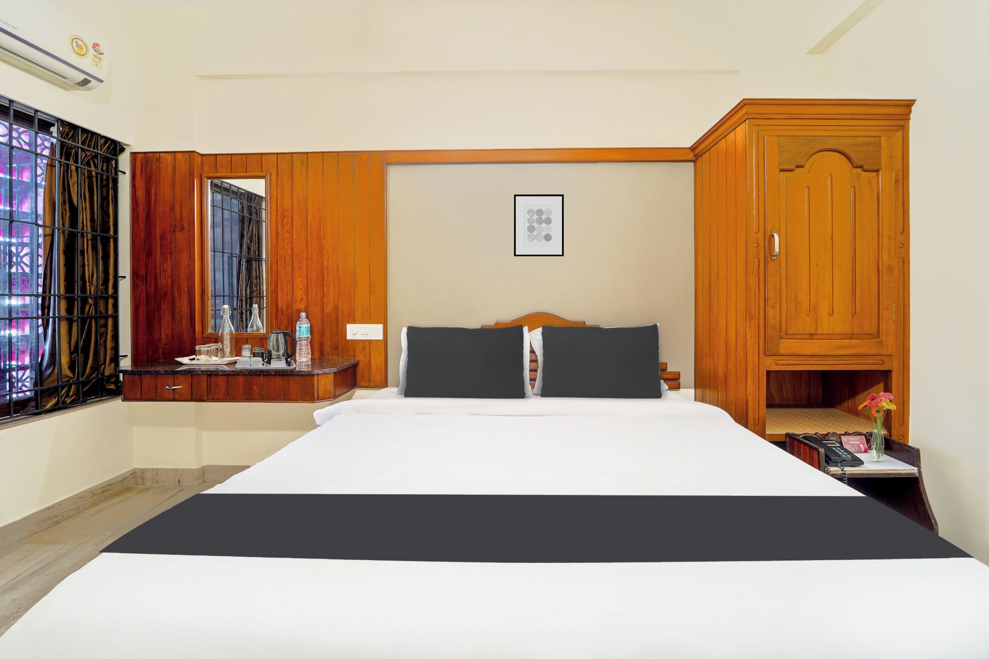Quarto de hotel com uma cama grande, um guarda-roupa de madeira, uma pequena mesa com chaleira e chávenas, e uma janela com cortinas.