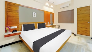 A hotel room with a large bed, a wooden headboard, a bedside table with a phone and a vase of flowers, a mirror, a wardrobe, and a wall-mounted air conditioning unit.