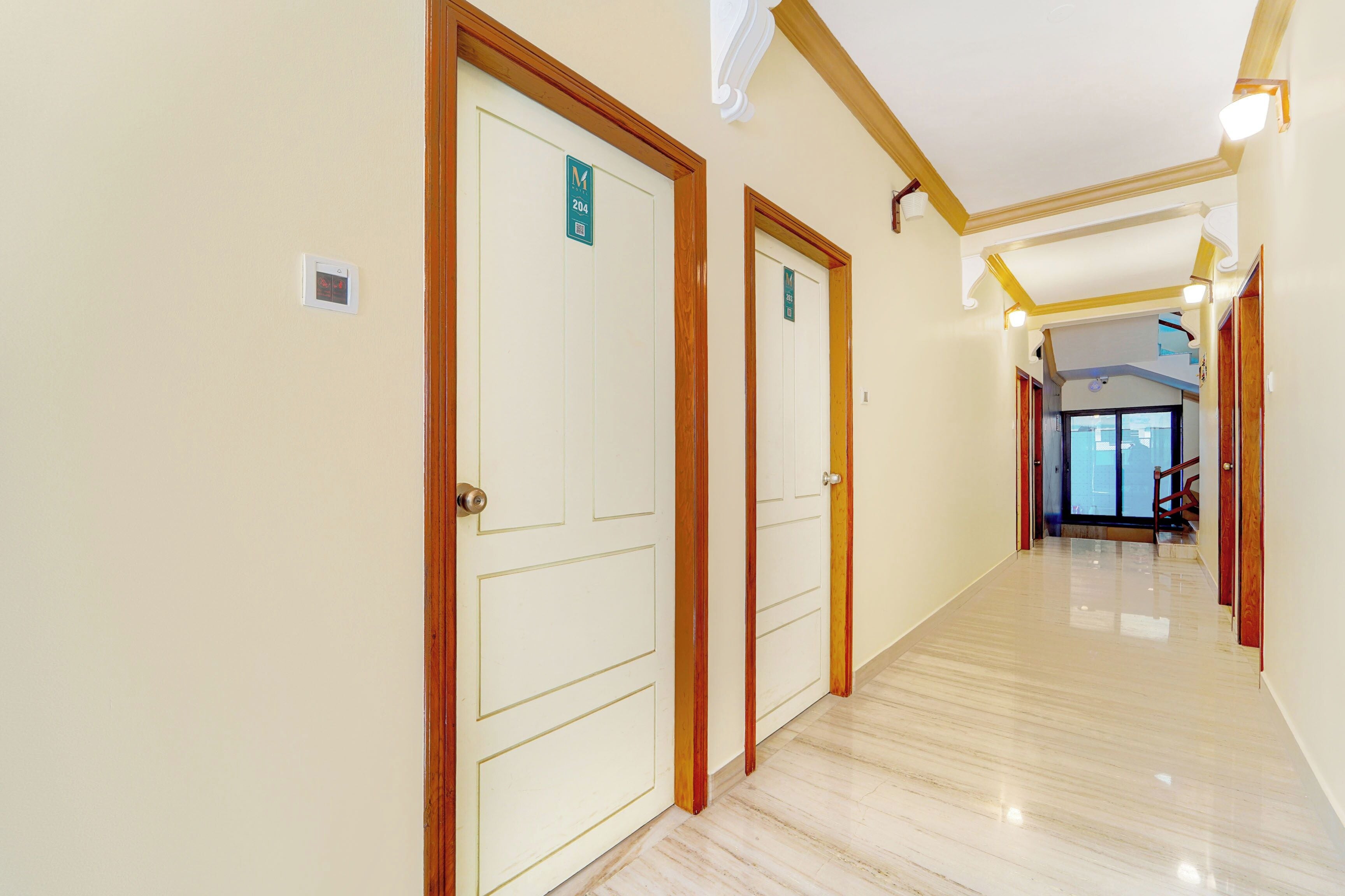 A hotel corridor with doors marked 204 and 203, a polished floor, and a view of the lobby area.