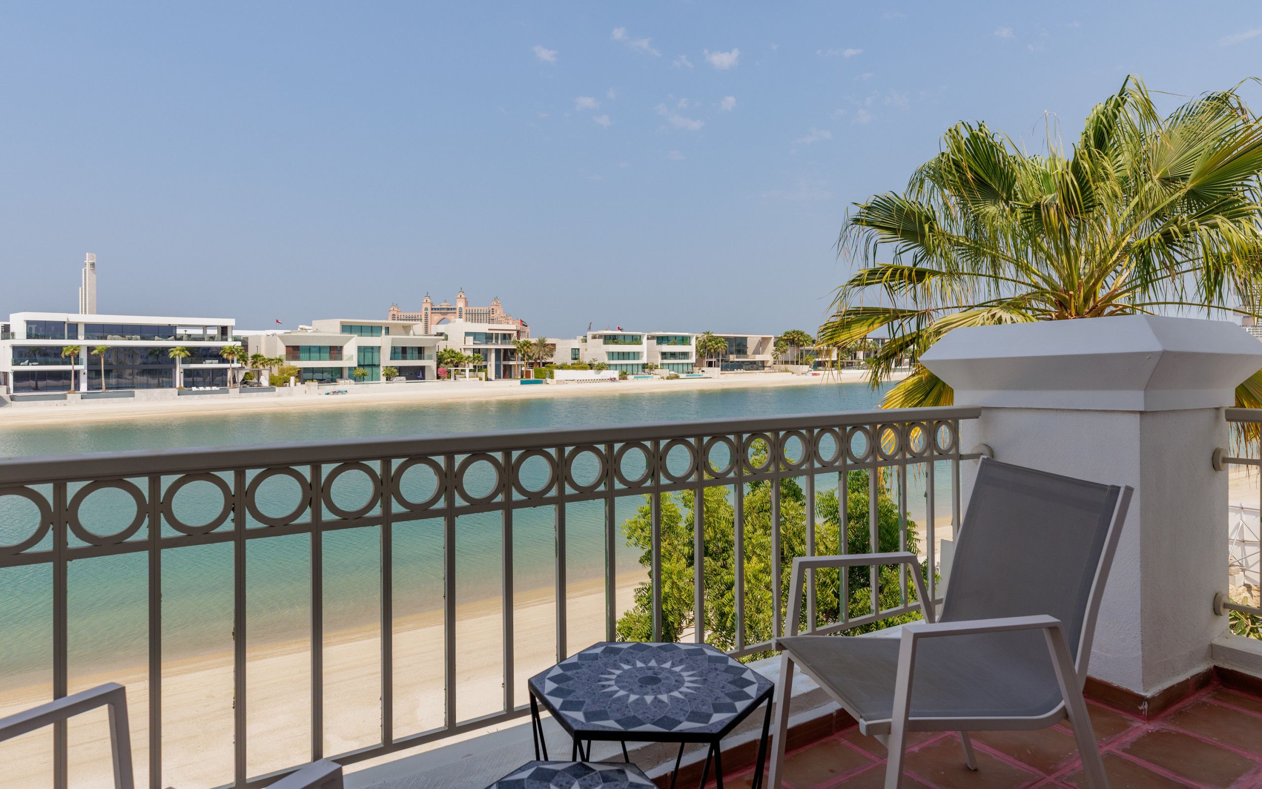 A balcony with a view of a beach, a pool, and hotel buildings in the background.
