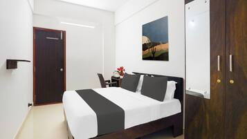 Habitación de hotel con cama, escritorio, silla, armario y un cuadro en la pared.