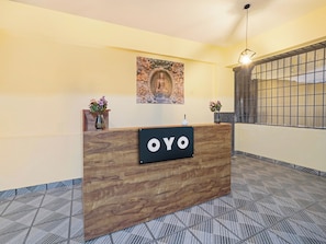 Un mostrador de recepción con un cartel que dice 'OYO' en un interior moderno con suelo estampado y un elemento decorativo en la pared.
