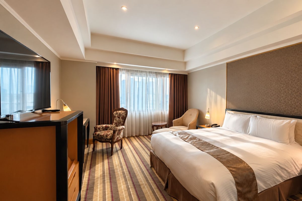 A hotel room with a bed, two chairs, a desk, and a television.
