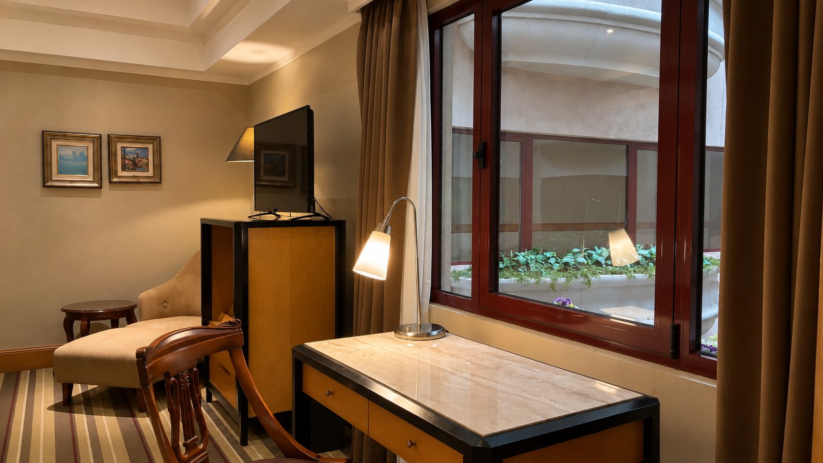 Habitació d'hotel amb escriptori, cadira, làmpada i finestra amb cortines.