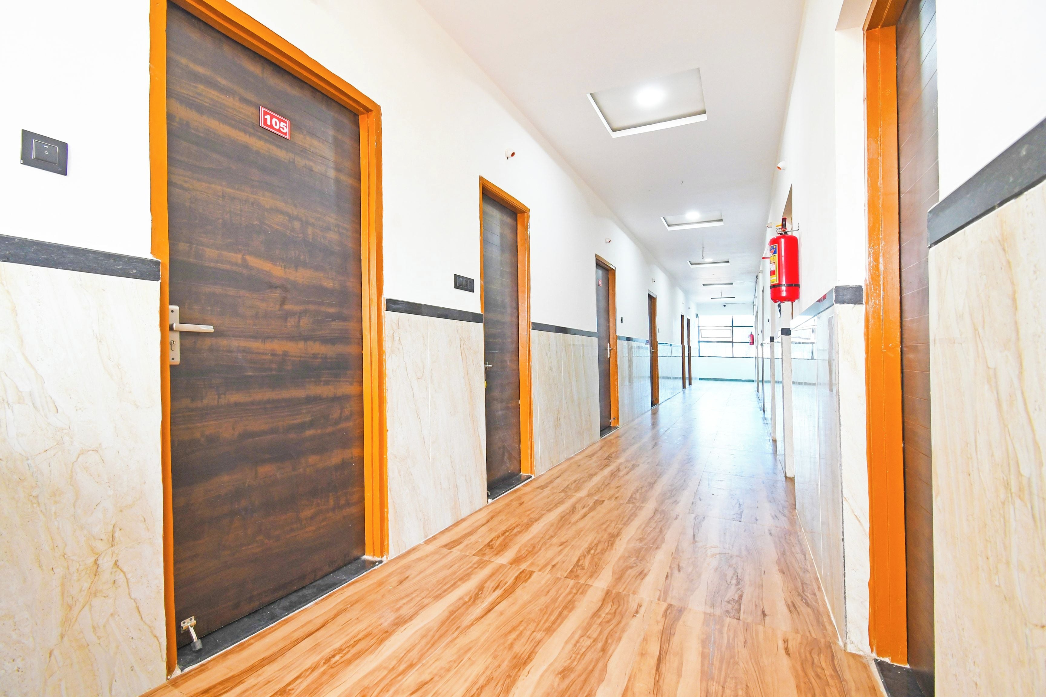 Corredor de hotel com piso de madeira, portas e extintor de incêndio.