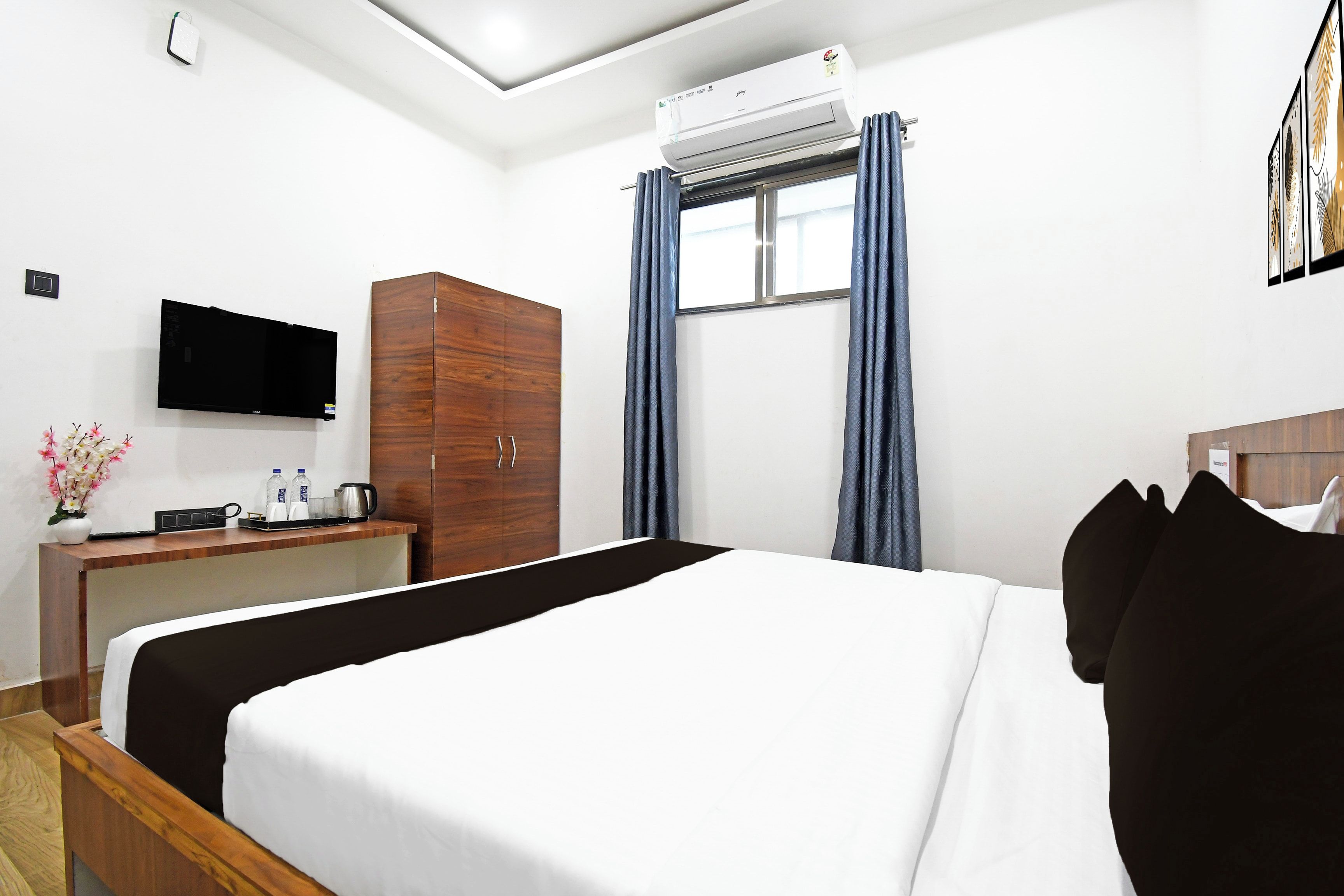 A hotel room with a bed, a desk with a flat-screen TV, a wardrobe, and a window with curtains.