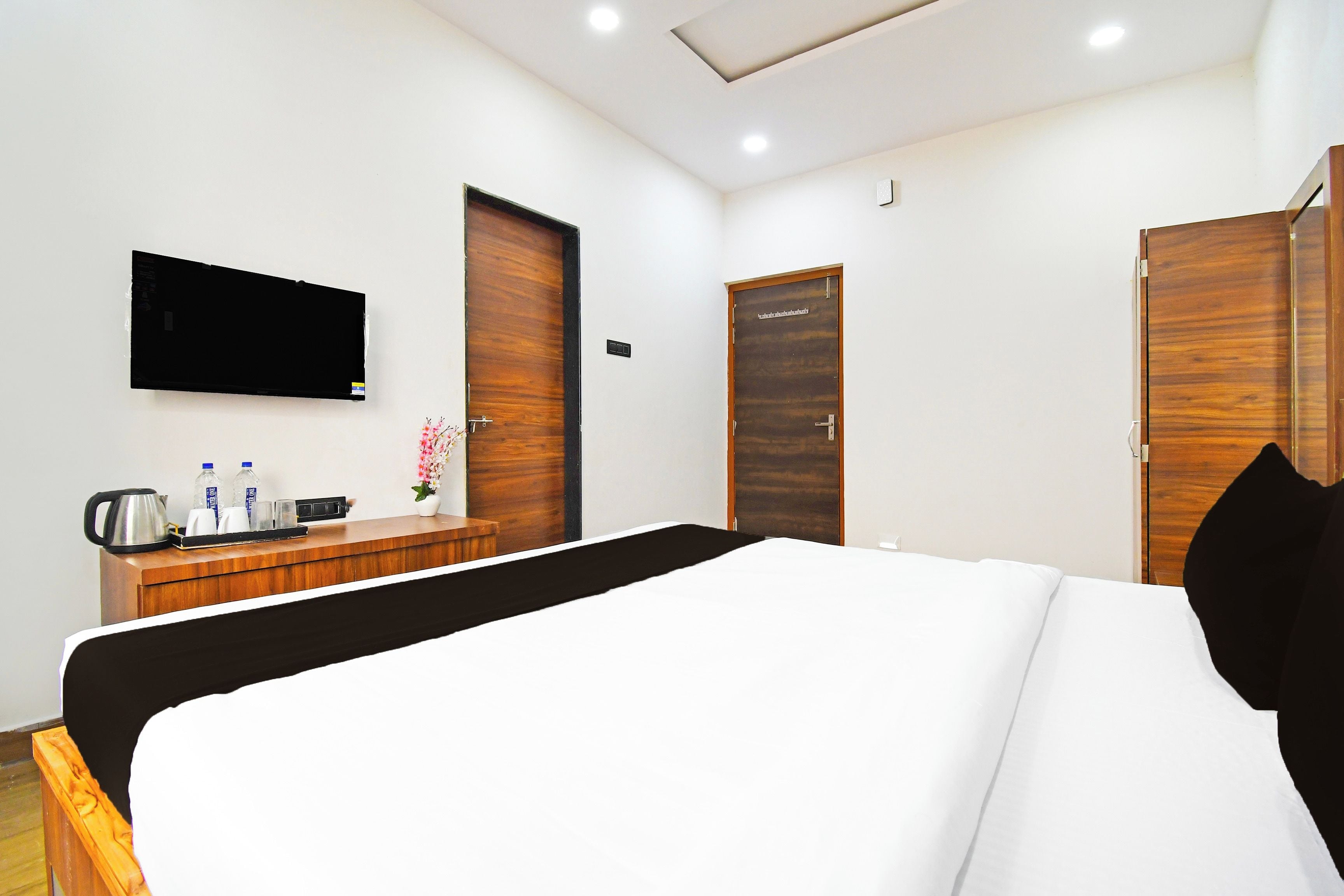 A hotel room with a bed, a TV mounted on the wall, a wooden dresser, and two doors.