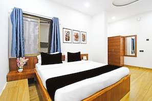 Quarto de hotel com cama, mesa de cabeceira, um vaso de flores, janela com cortinas e decoração nas paredes.