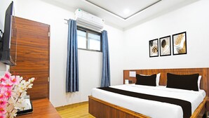 Hotellihuone, jossa on puinen sänky, litteänäyttöinen televisio, ikkuna, jossa on verhot, ja seinällä on kolme kehystettyä kuvaa.