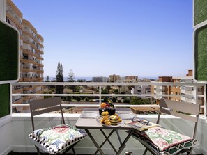 A balcony with a table set for two, overlooking a cityscape and the sea. - Sunstay Loft Saltillo (Torremolinos)