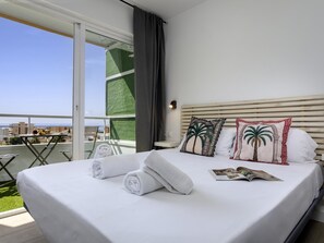 A hotel room with a bed, pillows, a magazine, and a view of the outside. - Sunstay Loft Saltillo (Torremolinos)