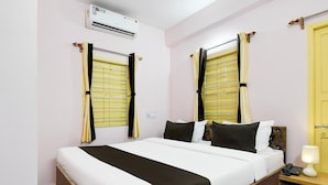 A hotel room with a bed, curtains, an air conditioning unit, a bedside table with a lamp, and a telephone. - Hotel O Ecopark Kolkata (Barasat)
