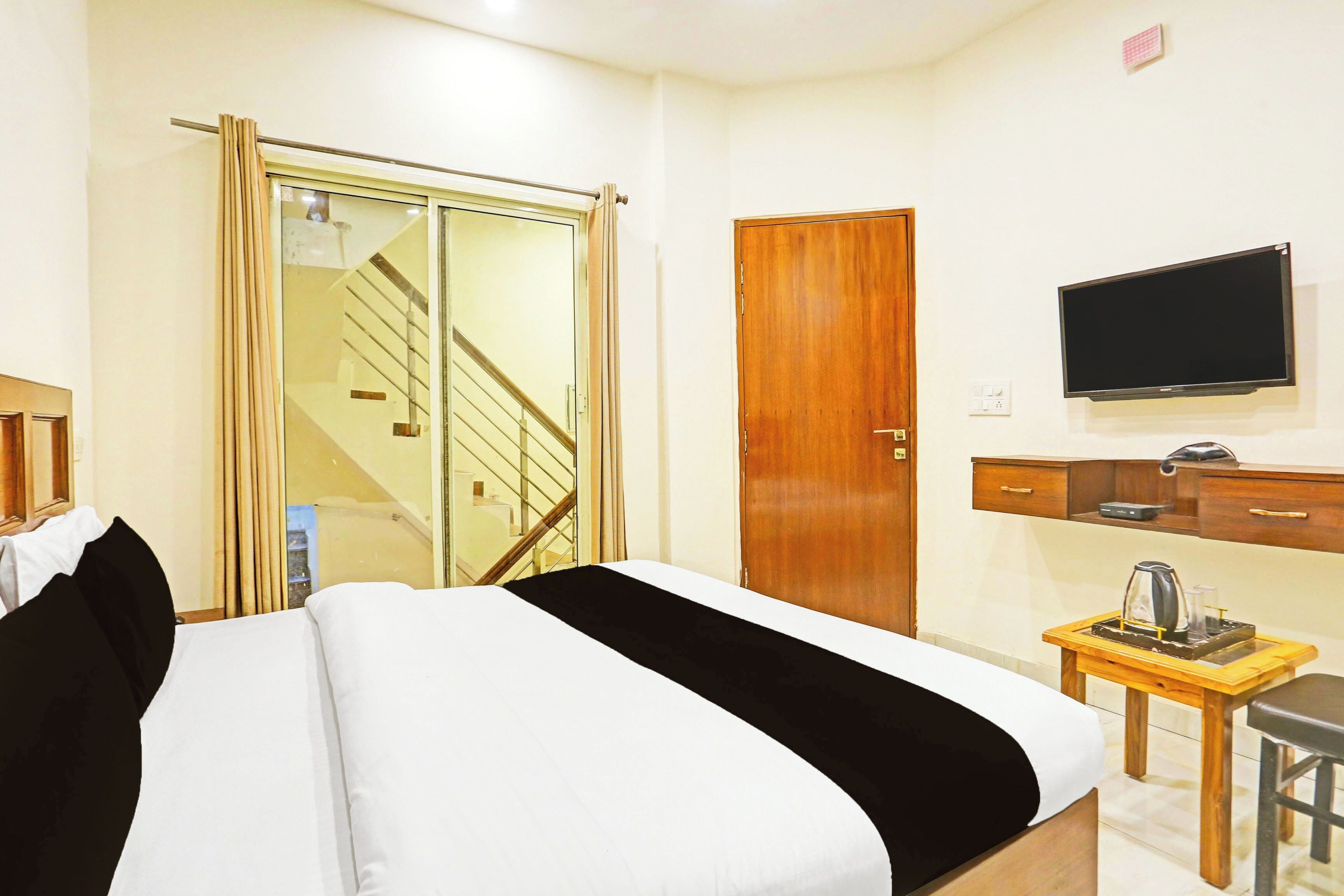 A hotel room with a bed, a TV, a wooden wardrobe, a desk with a kettle, and a staircase.