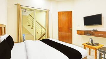A hotel room with a bed, a TV, a wooden wardrobe, a desk with a kettle, and a staircase.