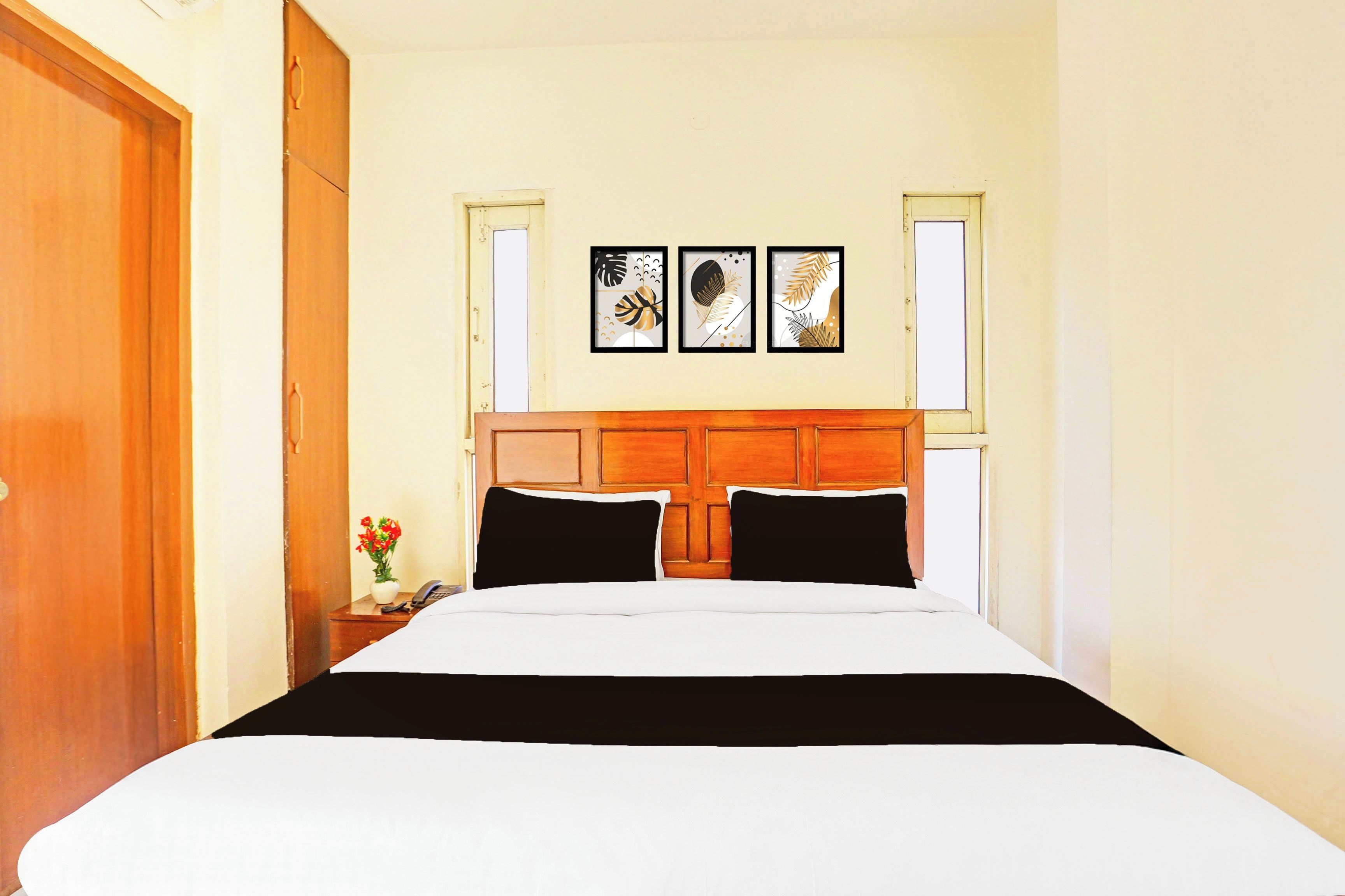 A hotel room with a bed, a nightstand, a vase with flowers, and two framed pictures on the wall.