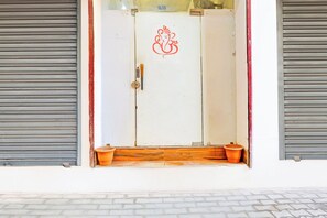 A white door with a red emblem, flanked by two grey roller shutters, and a wooden step leading to the entrance.