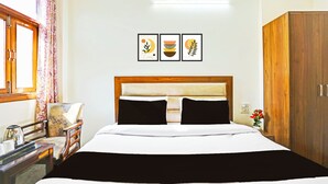 Hotellihuone, jossa on sänky, puinen vaatekaappi, työpöytä tuolilla ja ikkuna, jossa on verhot.