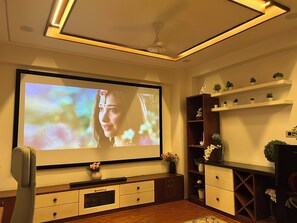 Una sala de estar con un televisor de pantalla plana grande montado en la pared, armarios de madera, una mesita con un florero y un ventilador de techo.