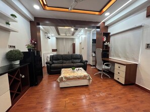 A modern living room with a leather sofa, a coffee table, and a TV. There are shelves with plants and a desk with a chair. - Cozy 1-bedroom apartment in beautiful Hyderabad with AC (Hyderabad)