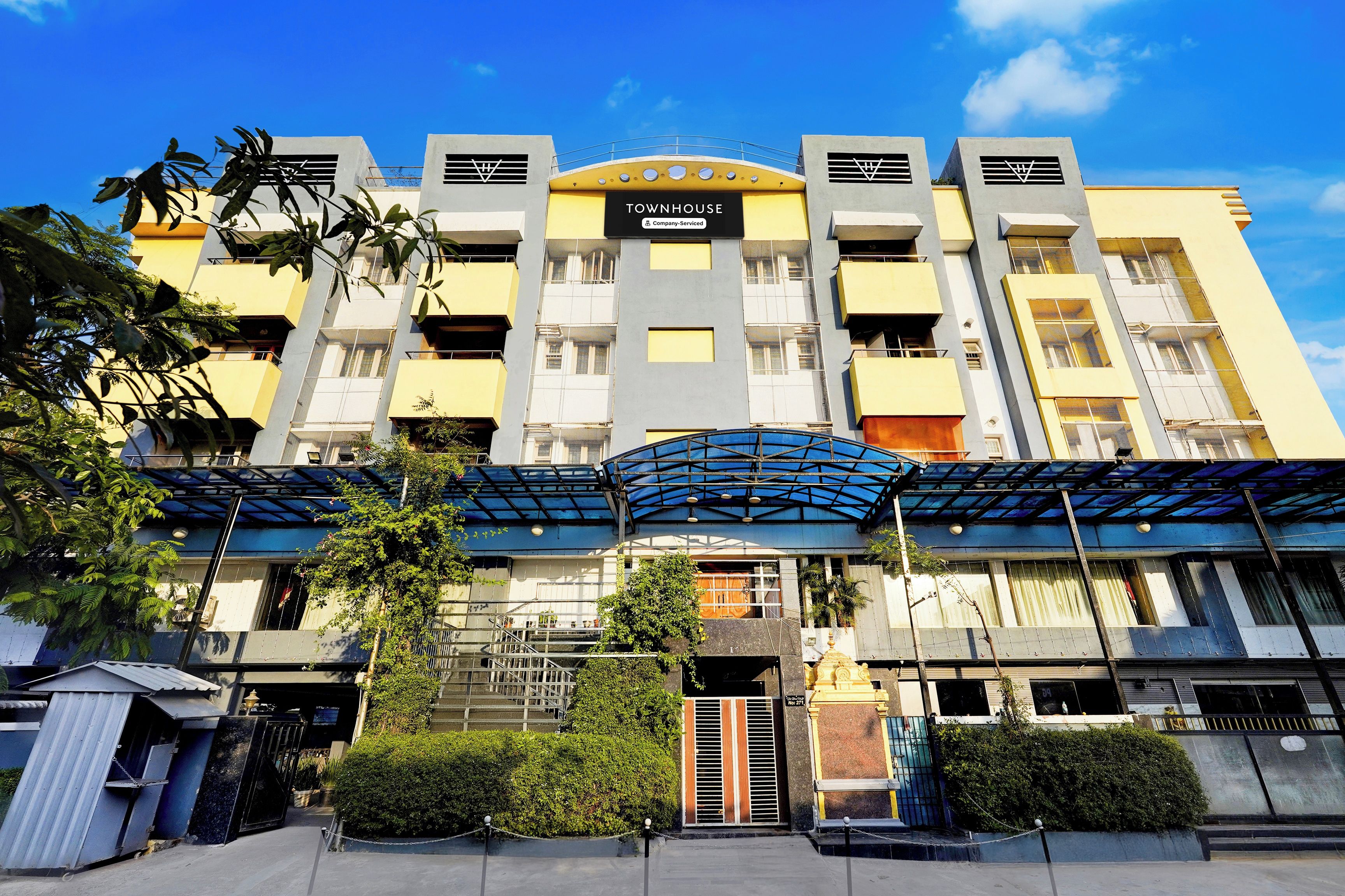A multi-story building with a prominent entrance, balconies, and a covered area with a blue roof.