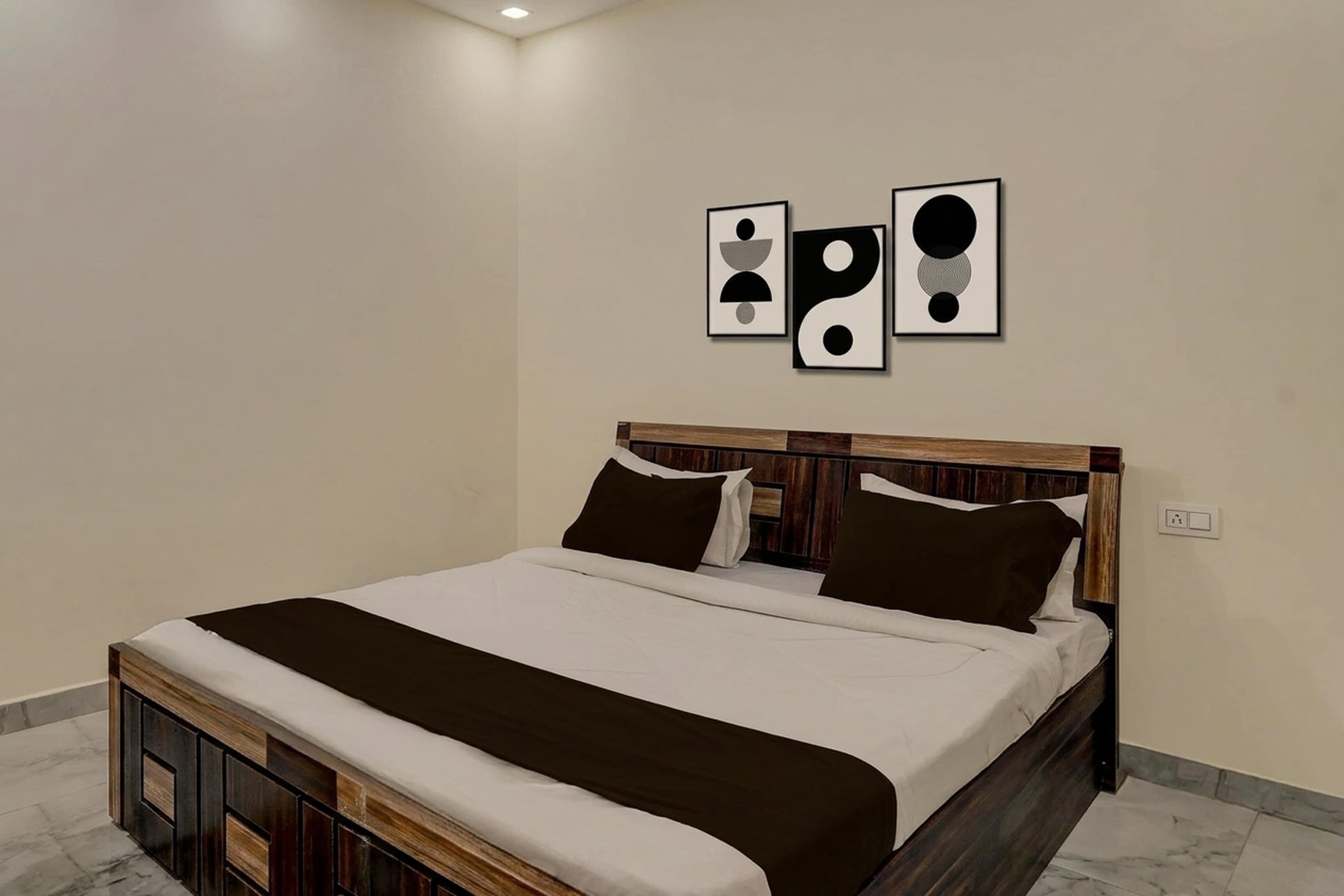 A bedroom with a wooden bed frame, white bedding, and three abstract wall art pieces.