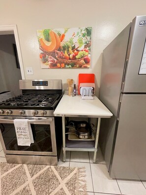 Una cocina con estufa de acero inoxidable, un refrigerador, un microondas y un cuadro en la pared con frutas y verduras.