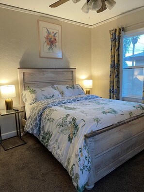 A bedroom with a wooden bed, two bedside lamps, a floral painting on the wall, and a window with curtains. - Cozy 1-bedroom apartment in peaceful Fresno with AC (Fresno)