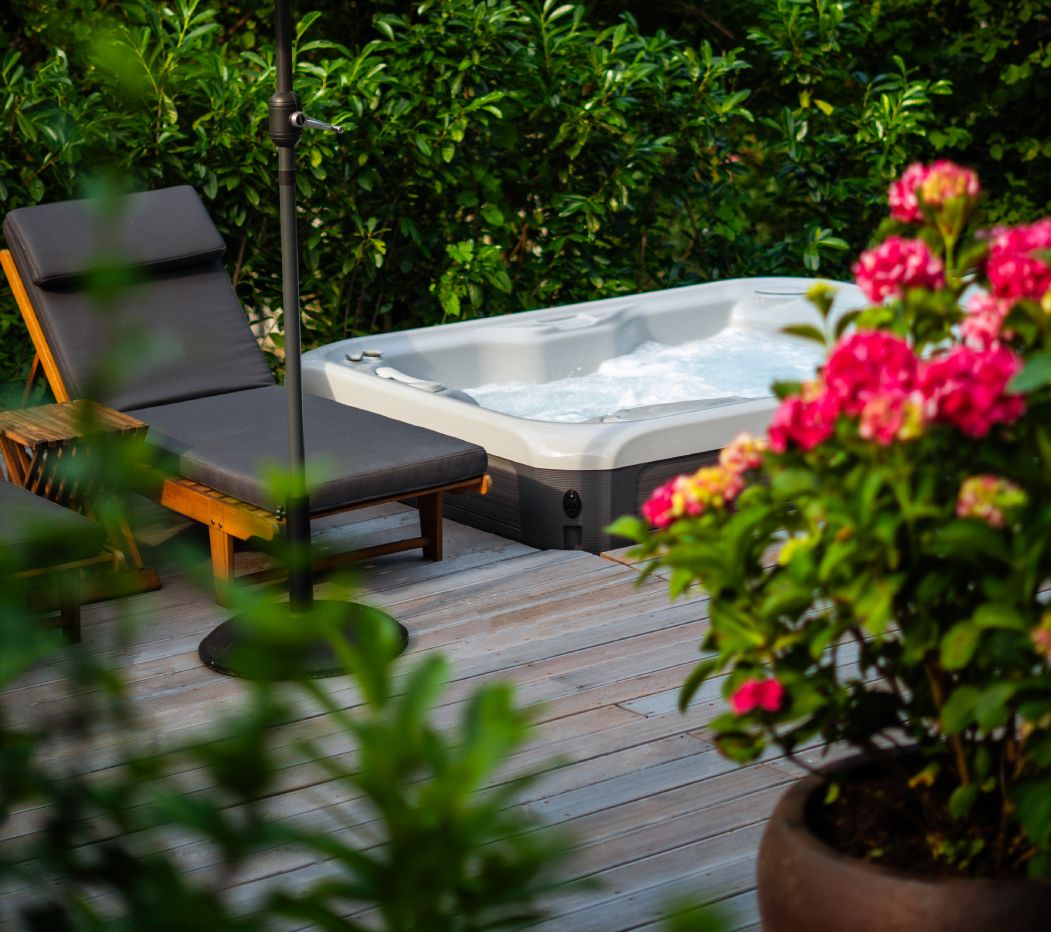 Una vasca idromassaggio su un pontile di legno, con poltroncine relax e vegetazione lussureggiante sullo sfondo.