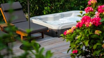 Una vasca idromassaggio su un pontile di legno, con poltroncine relax e vegetazione lussureggiante sullo sfondo.