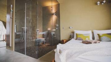Camera da letto con cabina doccia in vetro, un letto con cuscini e un comodino.