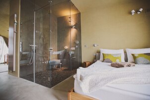 Un dormitorio con ducha de vidrio, una cama con almohadas y una mesita de noche.