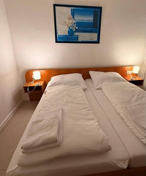 A hotel room with two beds, white linens, a painting above the beds, and bedside lamps. - Hotel G&k (Giesen)